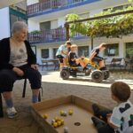 Oseba sedi ob kartonski škatli z žogicami, v ozadju se tri osebe vozijo na štirikolesnem vozilu na pedala.