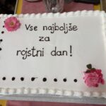 Bela pravokotna torta z rožnatimi cvetovi in napisom »Vse najboljše za rojstni dan!«.