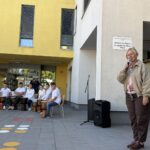 Ženska govori v mikrofon pred skupino sedečih oseb z bobni pri Osnovni šoli dr. Ljudevita Pivka Ptuj.