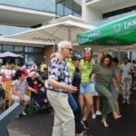 Več oseb pleše pred skupino sedečih ljudi na dvorišču.