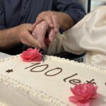 Dve osebi skupaj držita nož in režeta torto z napisom »100 let«.