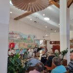 Otroci in odrasla glasbenica nastopajo s harmonikami in violinami pred sedečim občinstvom.