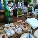 Na zunanji mizi so kruh z namazi, čebulo in češnjevim paradižnikom, steklenice ter skodelice.