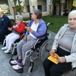 Skupina ljudi sedi na prostem in je prigrizke, dve osebi sedita na invalidskih vozičkih.