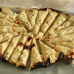 Pečena gibanica s svetlim nadevom in zapečenimi robovi je razrezana na trikotne kose.