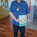 Moški z medaljo drži priznanje za »Met v tarčo – posamezno«.