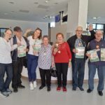 Skupina ljudi pozira z medaljami, priznanji in cvetjem po športnih igrah.