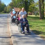 Skupina ljudi se v koloni premika po pločniku, nekateri na vozičkih in s svetlo modrimi baloni.