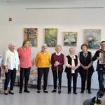 Skupina pevcev nastopa ob spremljavi harmonike pred sedečim občinstvom.