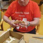 Stanovalec pri ustvarjalni delavnici s škarjami oblikuje koščke koruznega ličja.